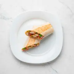 Kebab w tortilli przekrojony na pół, z widocznym kurczakiem i warzywami, na białym talerzu.