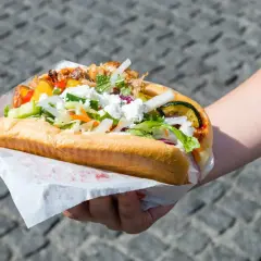 Kebab w bułce z kurczakiem i wołowiną, z warzywami i serem feta, trzymany w dłoni.