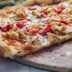 Kawałek domowej pizzy z kurczakiem i suszonymi pomidorami na kamieniu.