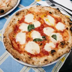 Pizza Margherita z roztopioną mozzarellą i bazylią na niebiesko-żółtym obrusie.
