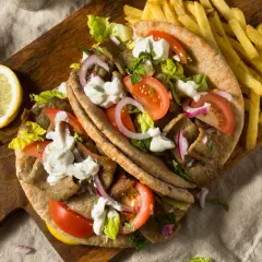 Pyszny kurczak gyros w picie z pomidorami, cebulą, sałatą i sosem. Obok frytki i cytryna.