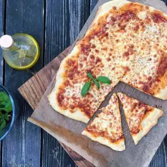 Pyszna margarita pizza z roztopionym serem i świeżą bazylią, obok butelka oliwy i miseczka ziół.