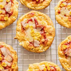 Mini pizze z serka wiejskiego, z kukurydzą i kawałkami mięsa, na metalowej kratce.