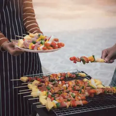 Ludzie grillują szaszłyki z mięsem i warzywami na grillu.