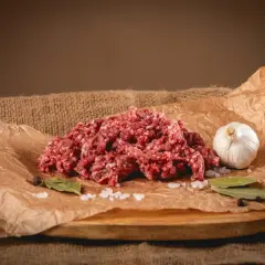 Świeże, mielone mięso wołowe, idealne na soczyste burgery. Obok czosnek, sól, liście laurowe i pieprz.