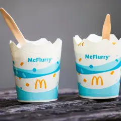 Dwa kubeczki McFlurry pistacjowe z drewnianymi łyżeczkami na drewnianym blacie.