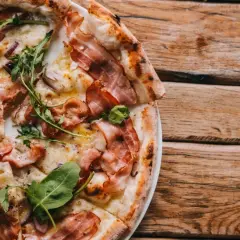 Pyszna pizza carbonara z chrupiącym boczkiem, rukolą i cebulą na drewnianym blacie.