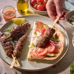 Pyszny, soczysty turecki kebab na talerzu z dodatkami: pitą, warzywami i jogurtowym sosem. Idealny na letni wieczór.