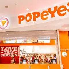 Wnętrze restauracji Popeyes Polska. Pracownicy za ladą, logo "Love That Chicken" i menu.