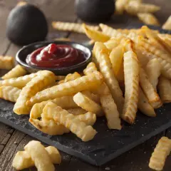Chrupiące frytki z karbowanej ziemniaków podane z ketchupem na czarnej desce.