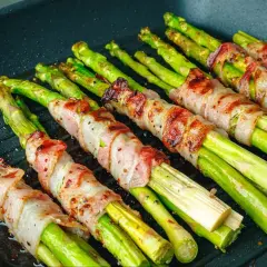 Zielone szparagi owinięte w boczek, grillowane na patelni. Pyszne szparagi z grilla gotowe do podania.