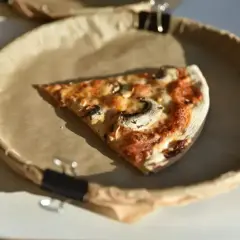 Kawałek pizzy z pieczarkami na papierowym talerzu. Zastanawiasz się nad pizza kcal?