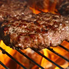 Soczyste kotlety mielone smażące się na grillu z płomieniami.