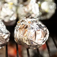 Ziemniaki z grilla zawinięte w folię aluminiową, piekące się nad żarem.