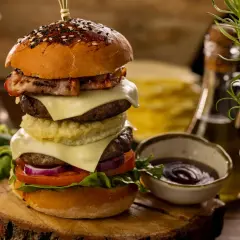 Wielowarstwowy burger wołowy z bekonem, serem, warzywami i sosem na drewnianej desce.