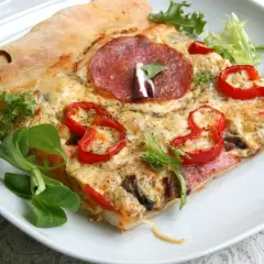Kawałek pizzy z salami, papryką i serem na białym talerzu.