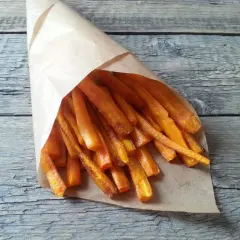 Chrupiące frytki z marchewki w papierowym rożku, ułożone na drewnianym blacie.