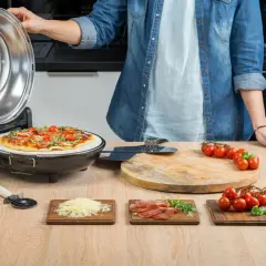 Osoba zamyka pokrywę pieca do pizzy, obok gotowa pizza i składniki.