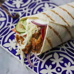 Pyszny kebab w picie z soczystym mięsem, chrupiącą kapustą, pomidorem, ogórkiem i czerwoną cebulą, podany na ozdobnym talerzu.