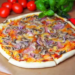 Pyszna pizza capriciosa z pieczarkami, szynką i czerwoną cebulą, gotowa do pokrojenia.