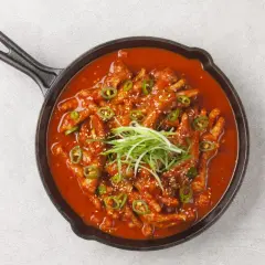 Kurczak w sosie gochujang, podany w żeliwnej patelni, ozdobiony zieloną cebulką i sezamem.