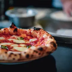 Puszysta pizza z serem i bazylią na ciemnym tle.