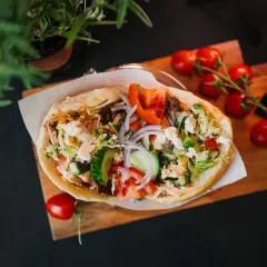 Pyszny kebab z warzywami i serem feta na desce, obok pomidorki i zielenina.