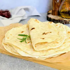 Stos świeżo upieczonych tortilli, idealnych do przygotowania najlepszej tortilli z ulubionymi dodatkami. Gałązka rozmarynu dodaje aromatu.