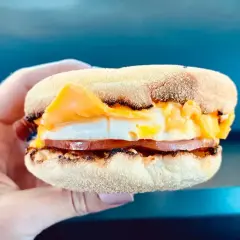 Mcmuffin farmerski z jajkiem, serem i szynką, trzymany w dłoni. Idealny na szybkie śniadanie.