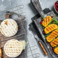 Dwa krążki sera camembert na grillu, jeden lekko roztopiony, obok grzanki i grillowane kawałki dyni z pestkami granatu.