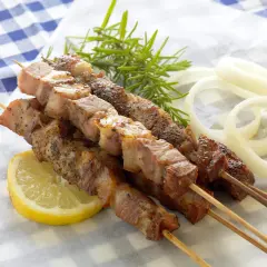 Aromatyczne souvlaki na patyczkach, podane z plasterkiem cytryny, gałązką rozmarynu i krążkami cebuli.