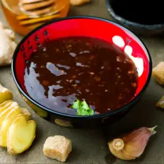 Miseczka z aromatycznym sosem teriyaki, obok świeży imbir, czosnek i brązowy cukier.