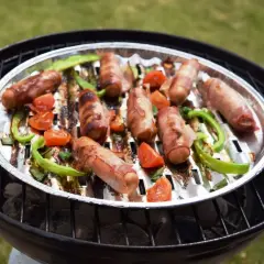 Pyszna kiełbasa na grilla, owinięta boczkiem, pieczona z papryką i pomidorkami na aluminiowej tacce.