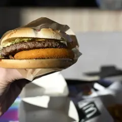 Dłoń trzyma burgera McDouble z podwójnym kotletem i chrupiącą warstwą.