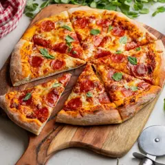 Apetyczna pizza pepperoni na drewnianej desce, ozdobiona listkami bazylii. Obok sos pomidorowy i czerwono-biała serwetka.