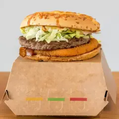 Drwal z chrzanem, czyli soczysty burger z chrupiącą panierką i wołowiną, na papierowym opakowaniu.