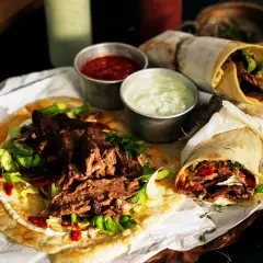 Pyszny lawasz kebab z soczystym mięsem, świeżą sałatą i sosami. Dwa zawinięte w papier i jeden otwarty na płaskim chlebie.