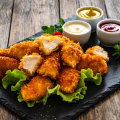 Chrupiące nuggetsy z kurczaka w złocistej panierce, podane z sosami i sałatą. Idealne na przekąskę!