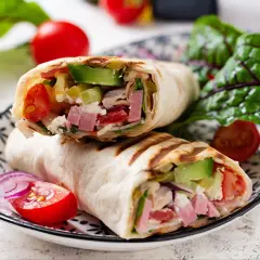 Pyszna tortilla z szynką i serem, pełna świeżych warzyw, podana na talerzu z pomidorkami i sałatą.