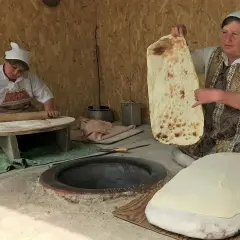 Kobieta pokazuje, co to jest lawasz – tradycyjny ormiański chleb. Obok druga kobieta wałkuje ciasto.