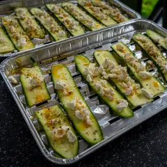 Półplasterki cukinii z serem feta i przyprawami, gotowe do grillowania.