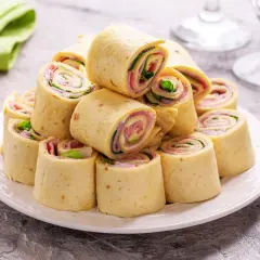 Szybkie przekąski z tortilli na zimno, zwinięte w rulony z szynką, serem i sałatą, ułożone na talerzu.
