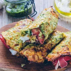 Złociste tortilla z cukinii, nadziewane serem, pomidorami i szynką, prezentowane na drewnianej desce.
