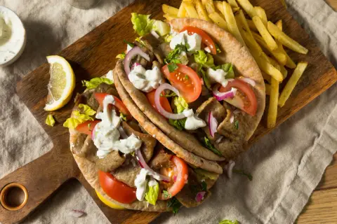 Pyszny kurczak gyros w picie z pomidorami, cebulą, sałatą i sosem. Obok frytki i cytryna.
