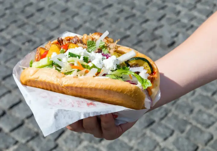 Kebab w bułce z kurczakiem i wołowiną, z warzywami i serem feta, trzymany w dłoni.