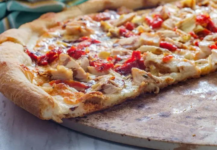 Kawałek domowej pizzy z kurczakiem i suszonymi pomidorami na kamieniu.