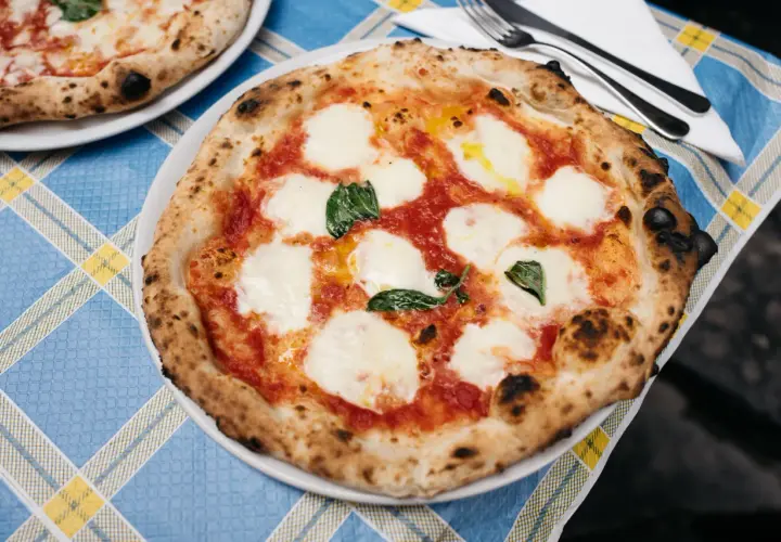 Pizza Margherita z roztopioną mozzarellą i bazylią na niebiesko-żółtym obrusie.
