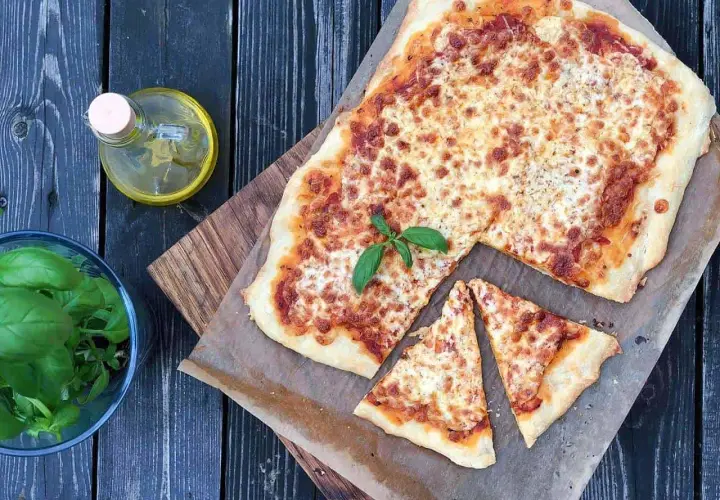 Pyszna margarita pizza z roztopionym serem i świeżą bazylią, obok butelka oliwy i miseczka ziół.