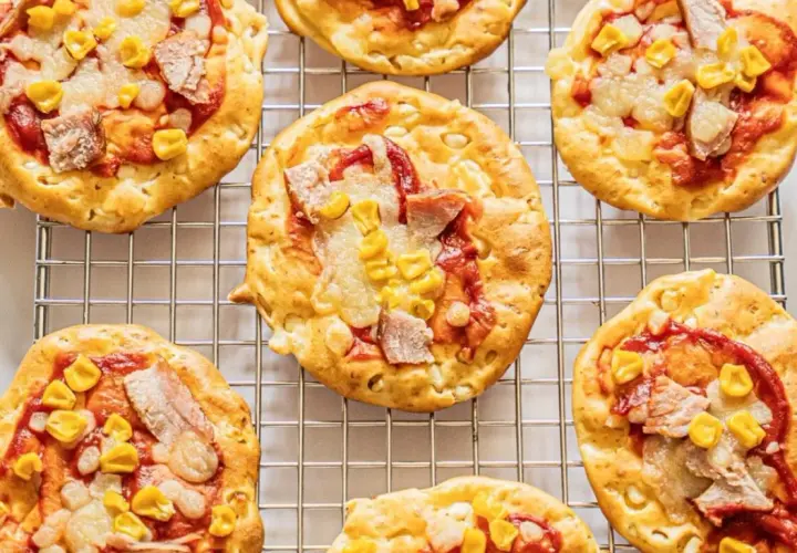 Mini pizze z serka wiejskiego, z kukurydzą i kawałkami mięsa, na metalowej kratce.
