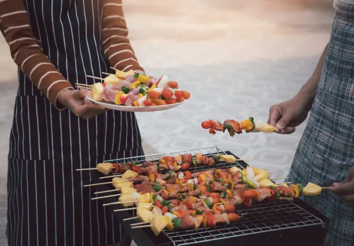 Ludzie grillują szaszłyki z mięsem i warzywami na grillu.